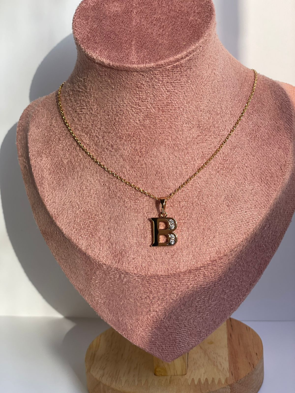 Collar dorado con dije de la letra B en estilo Clásico Serif, mostrado en un busto de exhibición.