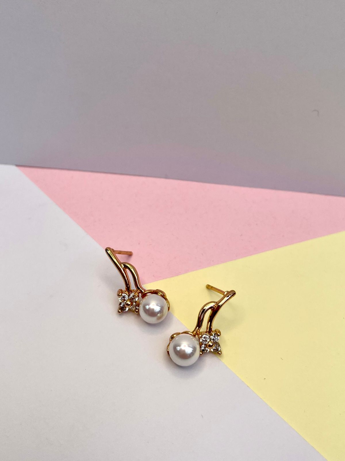 Aretes dorados con una perla de río central y tres pequeños cristales, presentados dentro de una caja de joyería color beige.