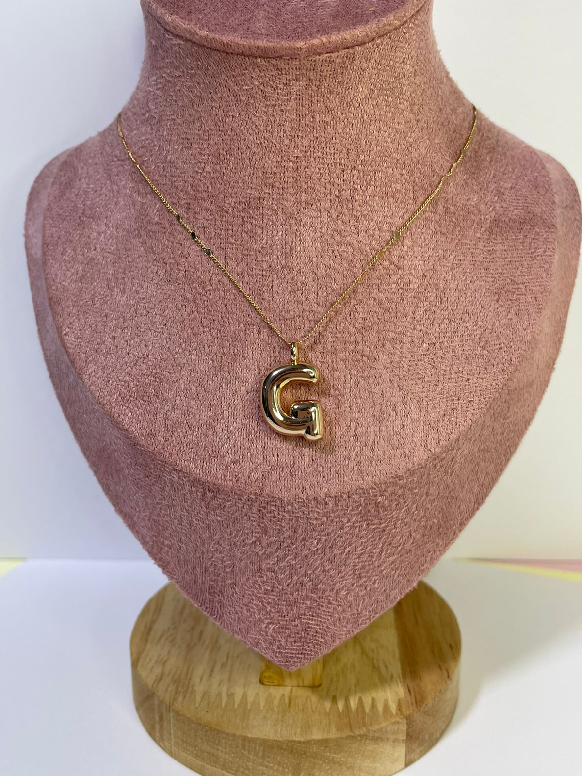Collar dorado con dije de la letra G en estilo Moderno Bold con cadena de puntos, mostrado en un busto de exhibición.