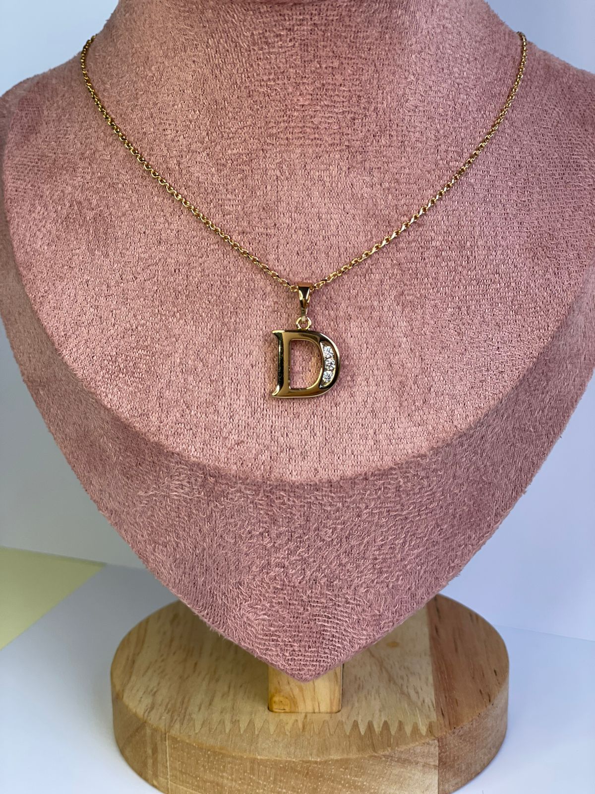 Collar dorado con dije de la letra D en estilo Clásico Serif mostrado en un busto de exhibición.