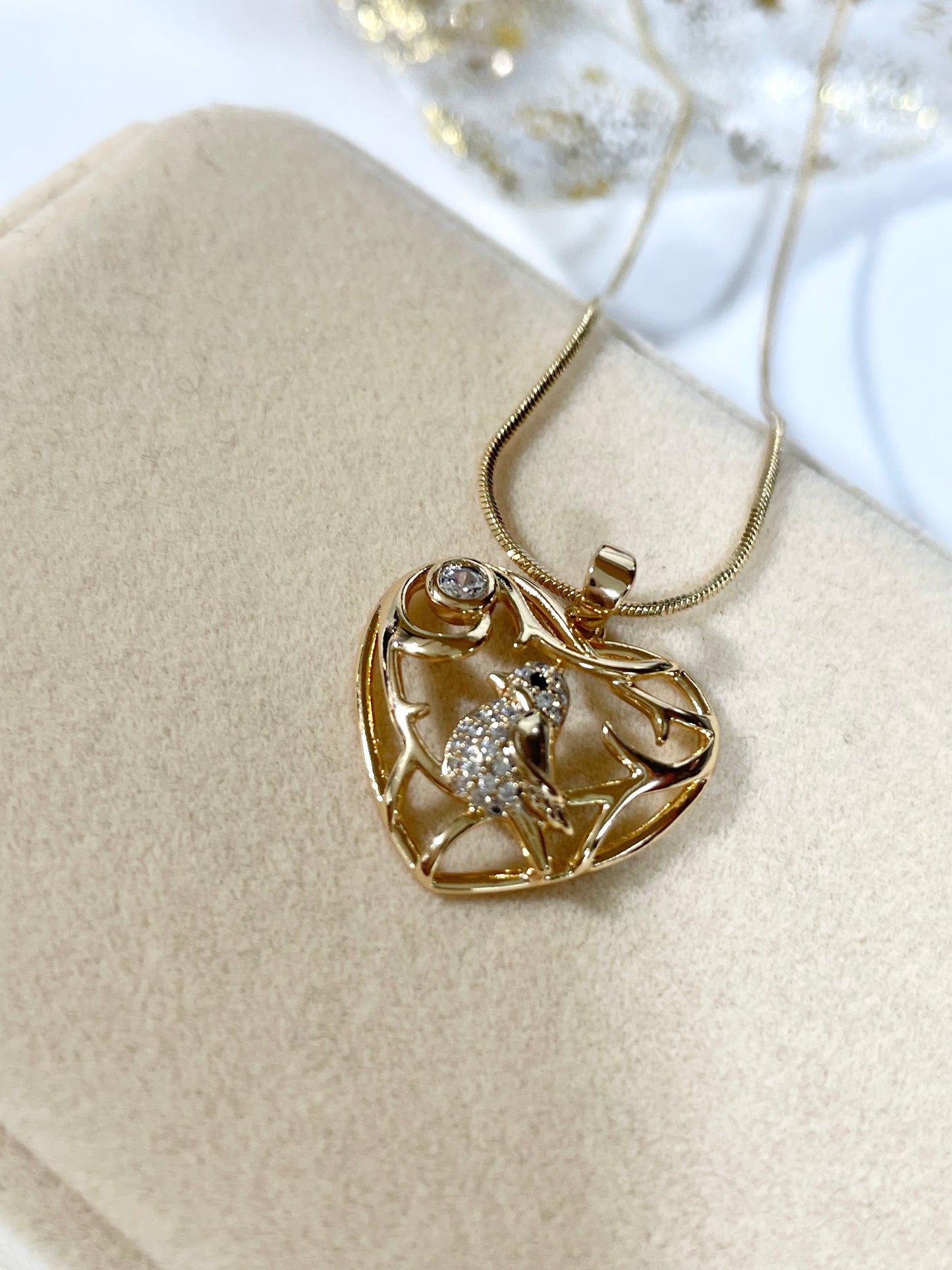 Collar dorado con cadena tipo serpiente y un dije en forma de corazón calado con un pájaro con incrustaciones de circones.