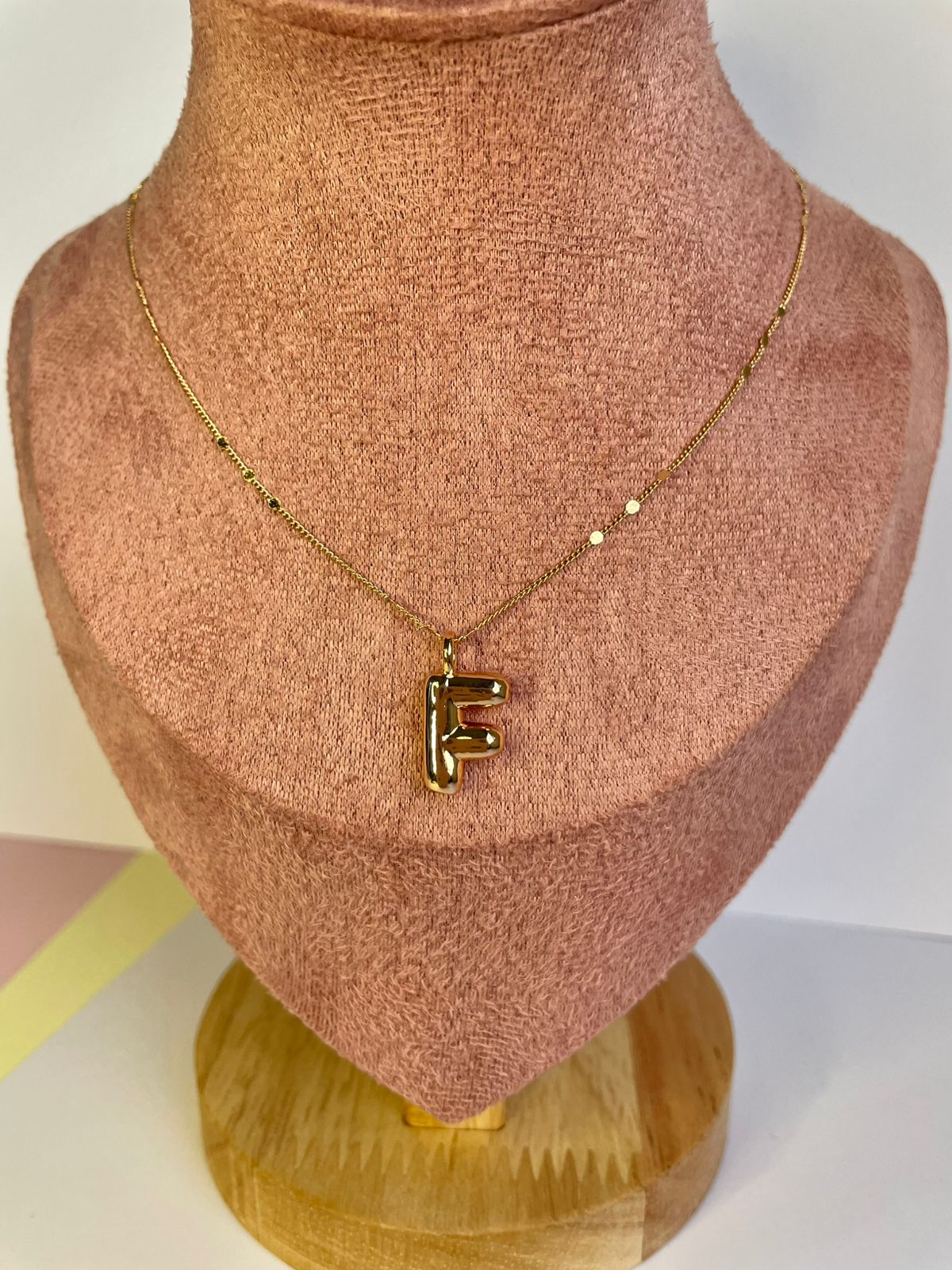 Collar dorado con dije de la letra F en estilo Moderno Bold con cadena de puntos, mostrado en un busto de exhibición.