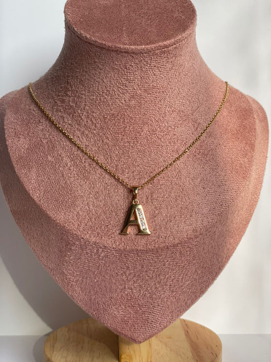 Collar dorado con dije de la letra A en estilo Clásico Serif, mostrado en un busto de exhibición.