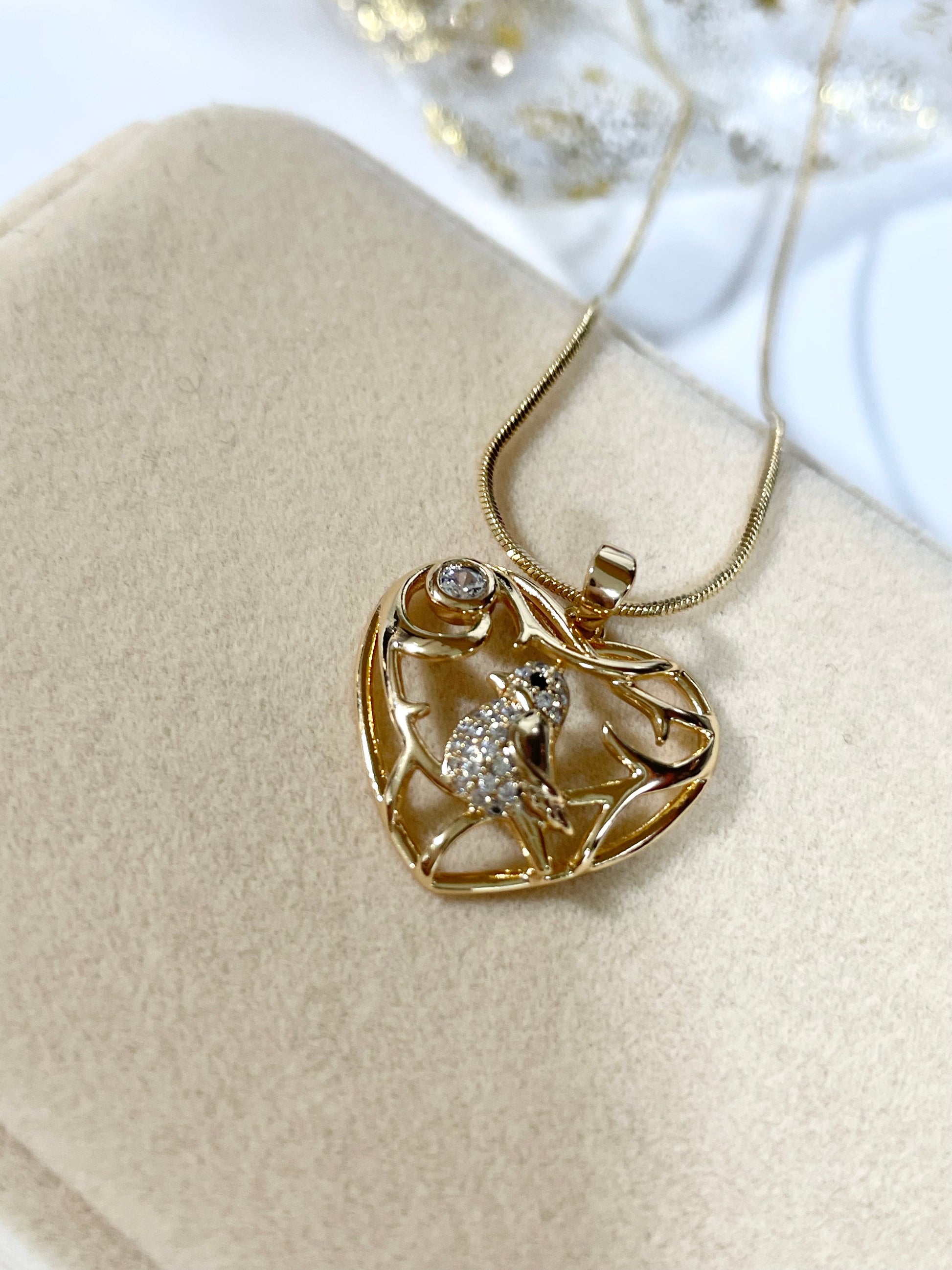 Collar dorado con cadena tipo serpiente y un dije en forma de corazón calado con un pájaro con incrustaciones de circones.
