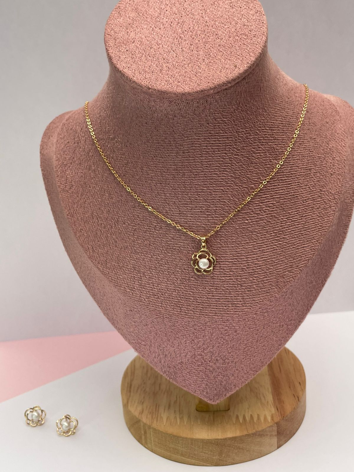 Set de joyas de collar y aretes con diseño de flor dorada y perla central, presentado en una elegante caja de joyería color beige.